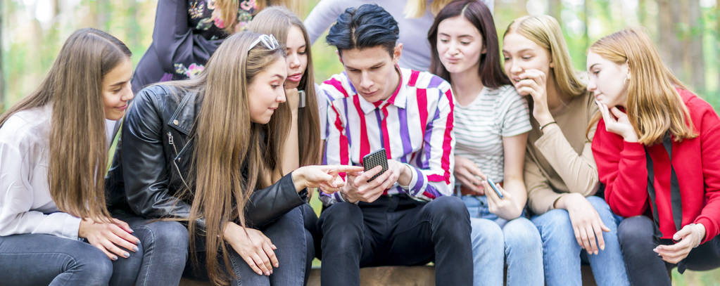 Nastolatkowie siedzą na ławce w lesie i patrzą na telefon. Suma - Zdjęcie, obraz