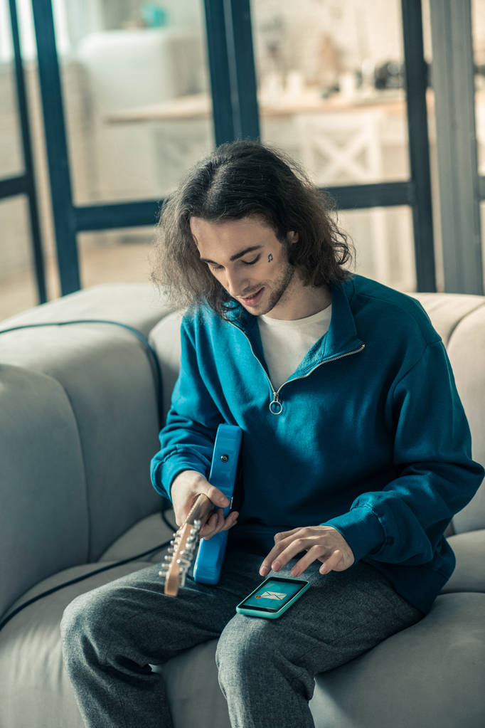 Ochotný mladý kytarista s dlouhými vlasy drží hudební nástroj - Fotografie, Obrázek