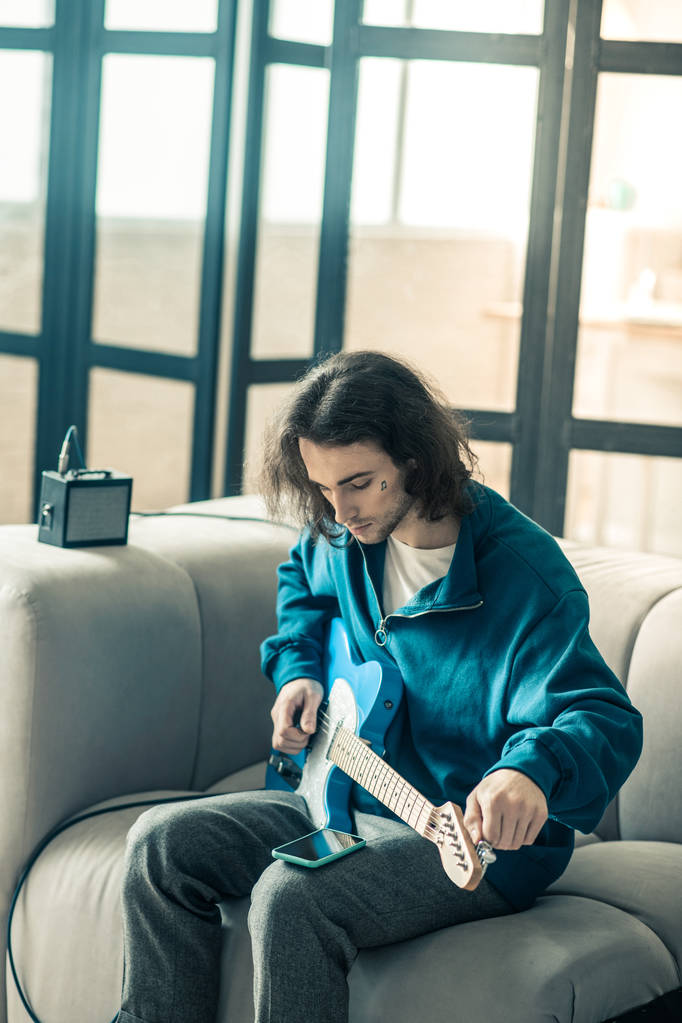 Dark-haired knappe jongen toning zijn elektronische gitaar en controleren van de sociale media - Foto, afbeelding