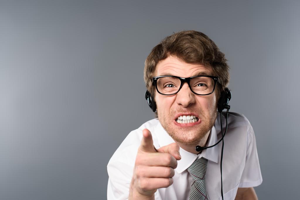 operador de call center irritado em fone de ouvido e óculos apontando com o dedo para a câmera
 - Foto, Imagem