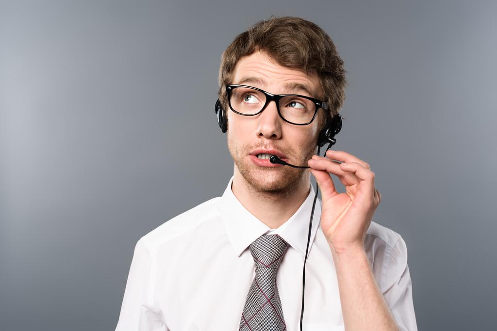álmodozó call center operátor fejhallgató és szemüveg keres el a szürke háttér - Fotó, kép