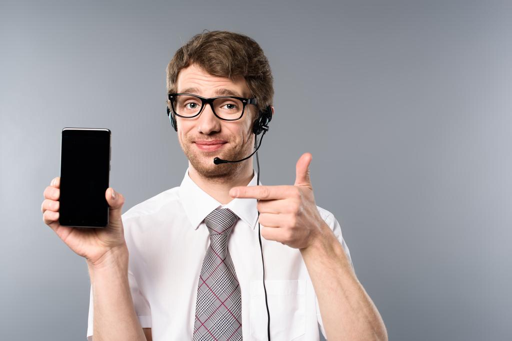 operatore di call center positivo in occhiali e auricolare che punta con il dito allo smartphone con schermo vuoto
 - Foto, immagini