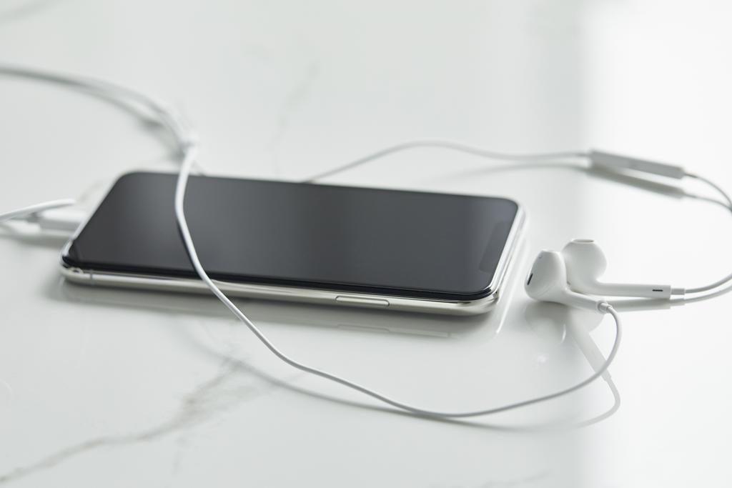селективная фокусировка смартфона с чистым экраном и проводными наушниками на белой поверхности
 - Фото, изображение