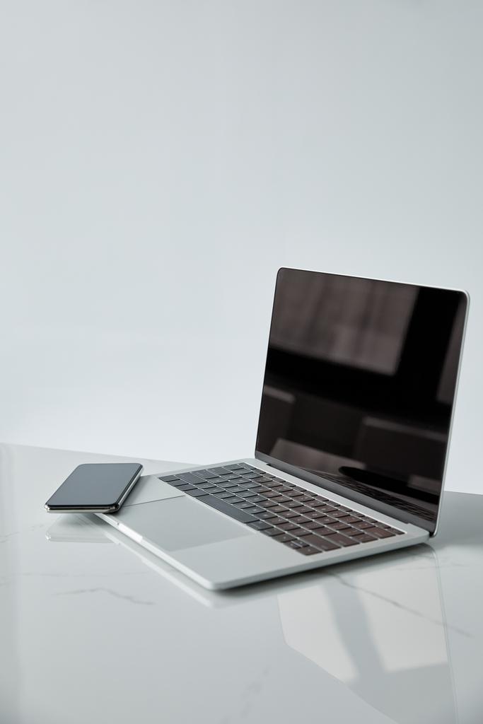 ordinateur portable et smartphone avec écran blanc sur surface blanche isolé sur gris
  - Photo, image