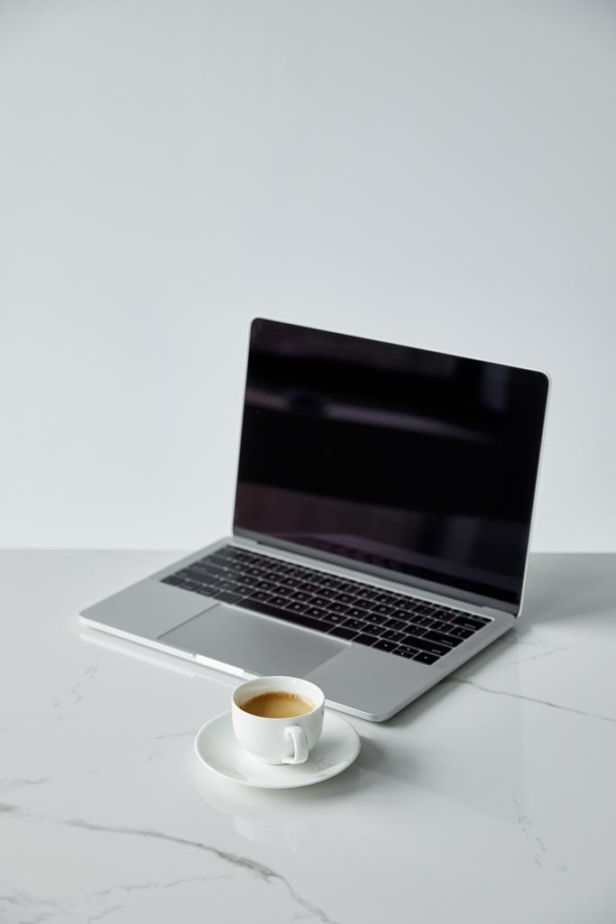 φορητό υπολογιστή με κενή οθόνη και μαύρο πληκτρολόγιο, και πιατάκι με φλιτζάνι καφέ απομονώνεται σε γκρι - Φωτογραφία, εικόνα