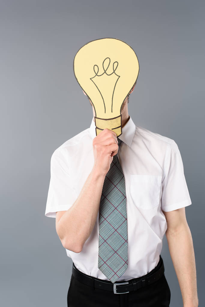 businessman holding paper cut light bulb in front of face on grey background - Photo, Image