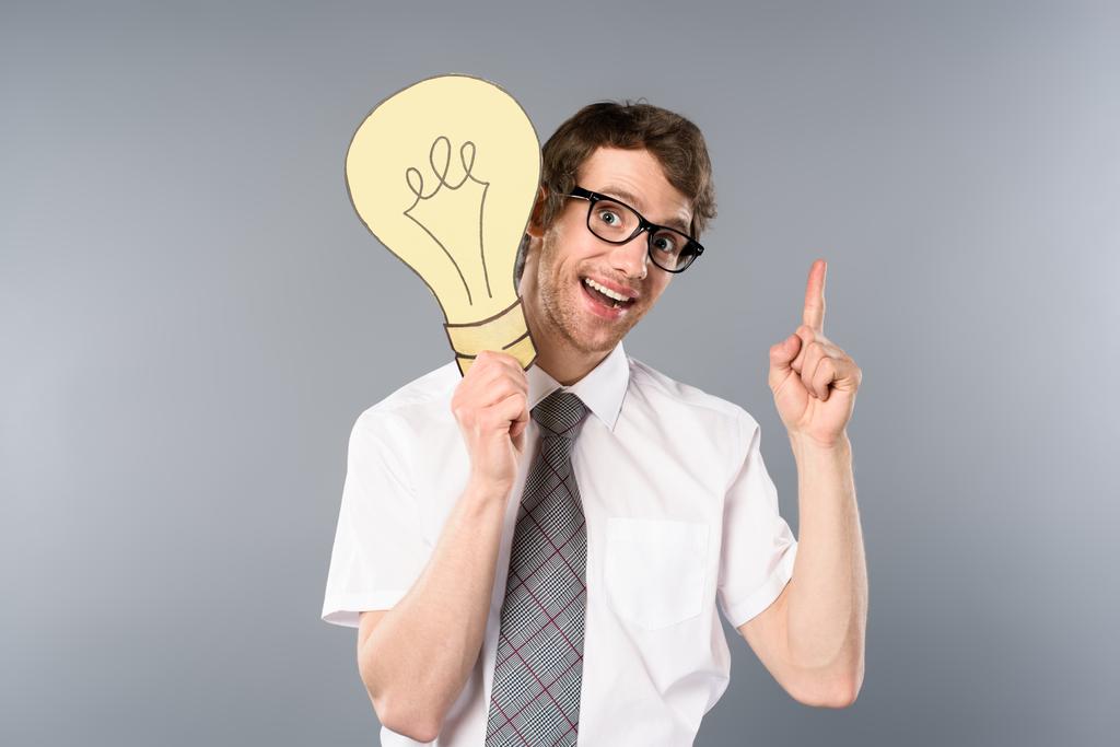 усміхнений бізнесмен в окулярах тримає жовту паперову розрізану лампочку і показує жест ідеї на сірому фоні
 - Фото, зображення