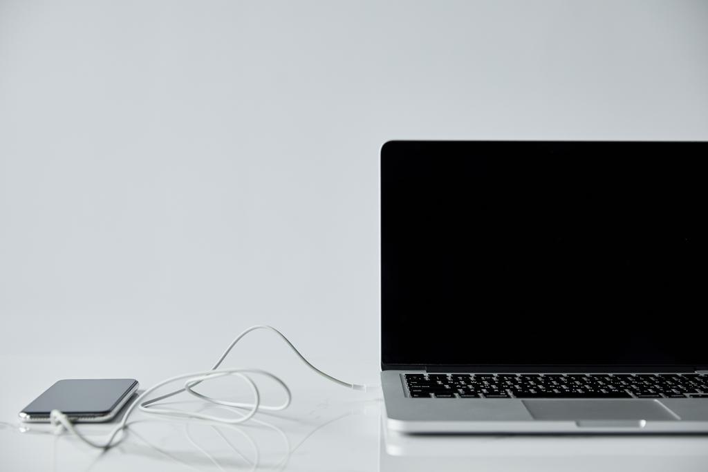 laptop con pantalla en blanco y smartphone con auriculares conectados aislados en gris
 - Foto, Imagen