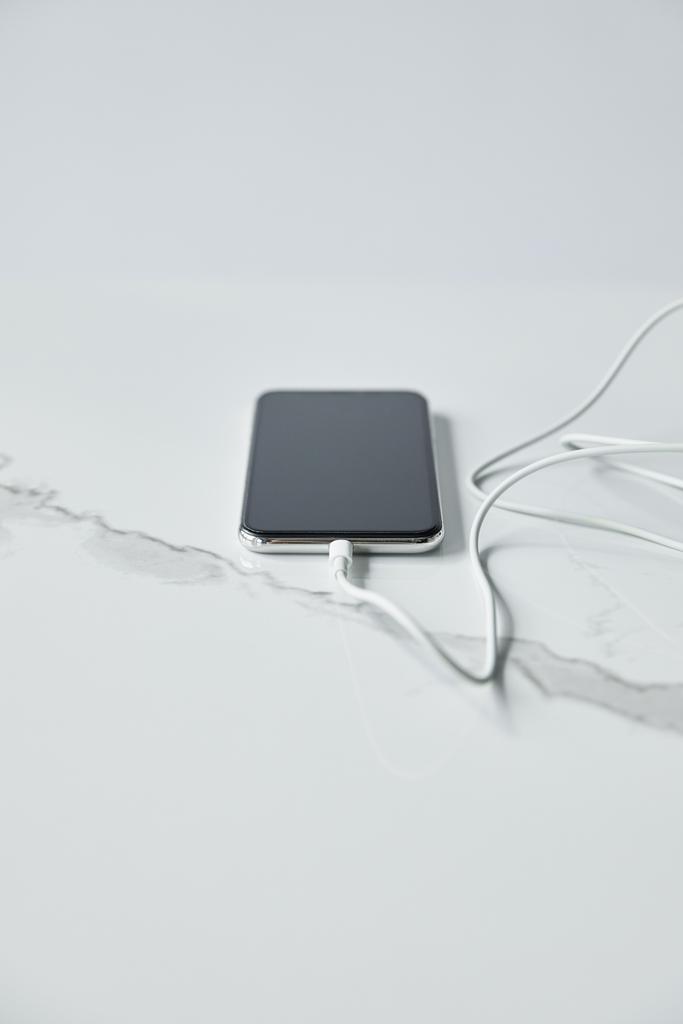 selectieve focus van smartphone met leeg scherm met aangesloten kabel geïsoleerd op grijs - Foto, afbeelding