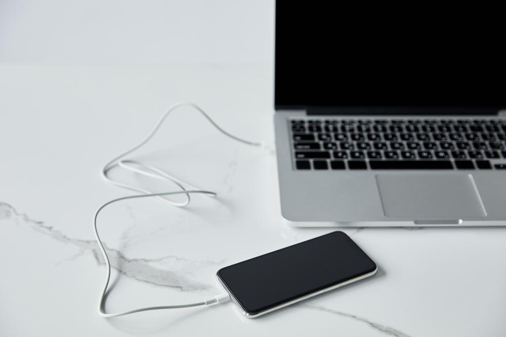 selectieve focus van smartphone in verband met kabel naar laptop met leeg scherm geïsoleerd op grijs - Foto, afbeelding
