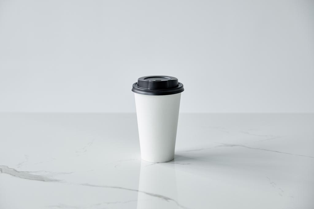 white paper cup with black cap on white marble surface isolated on grey - Photo, Image