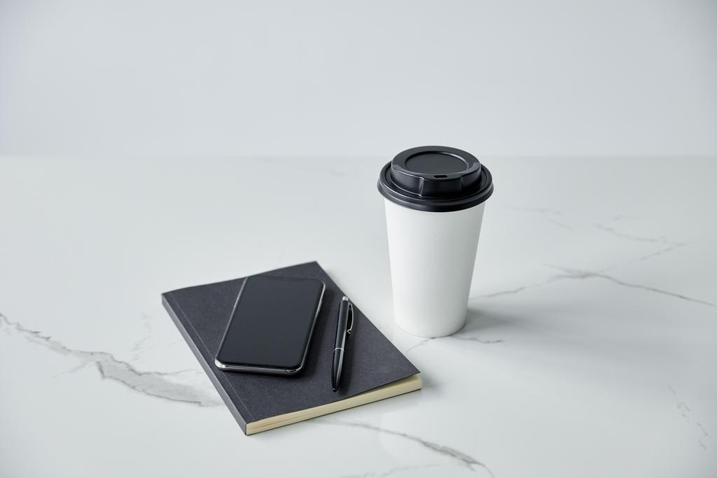 Smartphone mit leerem Bildschirm, schwarzem Notizbuch, Stift und Pappbecher isoliert auf grau - Foto, Bild