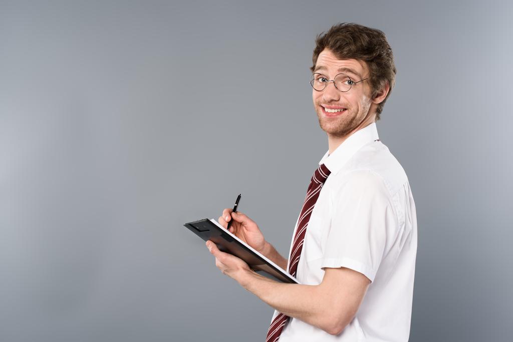 usmívající se muž podnikatel s perem psát ve schránce na šedém pozadí - Fotografie, Obrázek