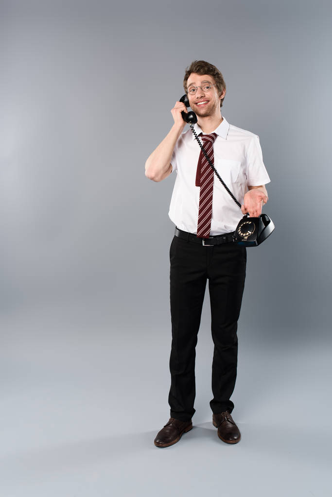усміхнений бізнесмен в окулярах говорить на старовинному телефоні на сірому
 - Фото, зображення