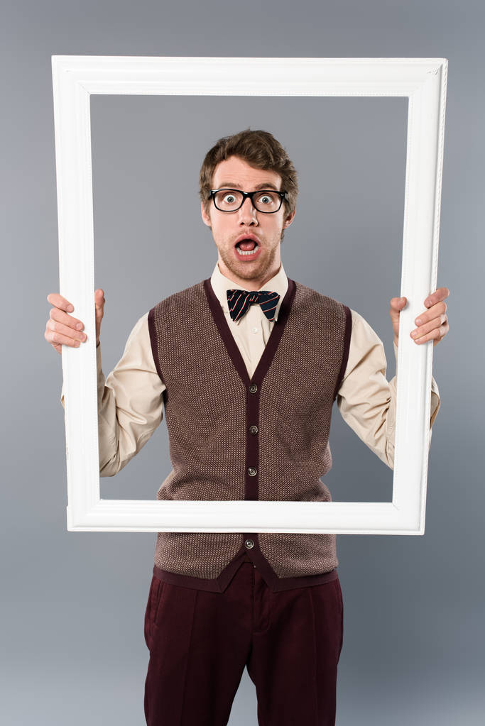 hombre sorprendido sosteniendo marco blanco sobre fondo gris
 - Foto, imagen