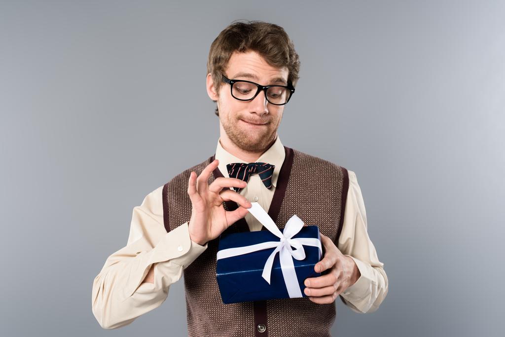 gracioso hombre en gafas desatando arco en caja de regalo sobre fondo gris
 - Foto, imagen