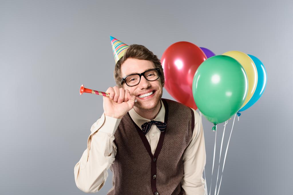 Χαμογελαστός άνθρωπος γυαλιά και κόμμα ΚΓΠ κρατώντας πολύχρωμα μπαλόνια και κόμμα κέρατο σε γκρίζο φόντο - Φωτογραφία, εικόνα