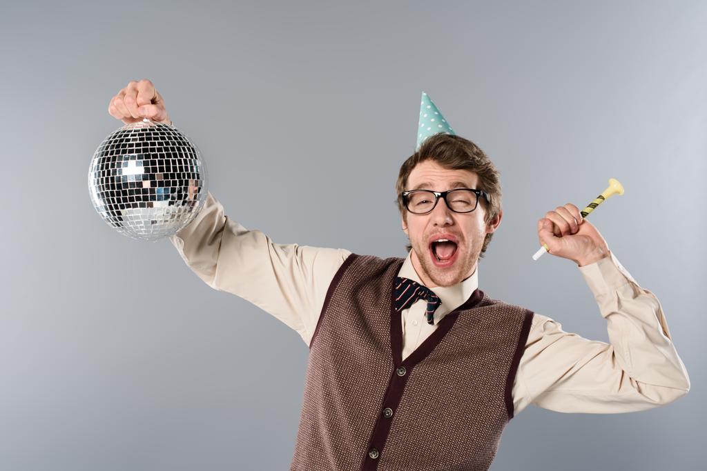 ενθουσιασμένος άνδρας στο καπάκι κόμμα κρατώντας λαμπερά μπάλα disco και κόμμα κέρατο σε γκρίζο φόντο - Φωτογραφία, εικόνα
