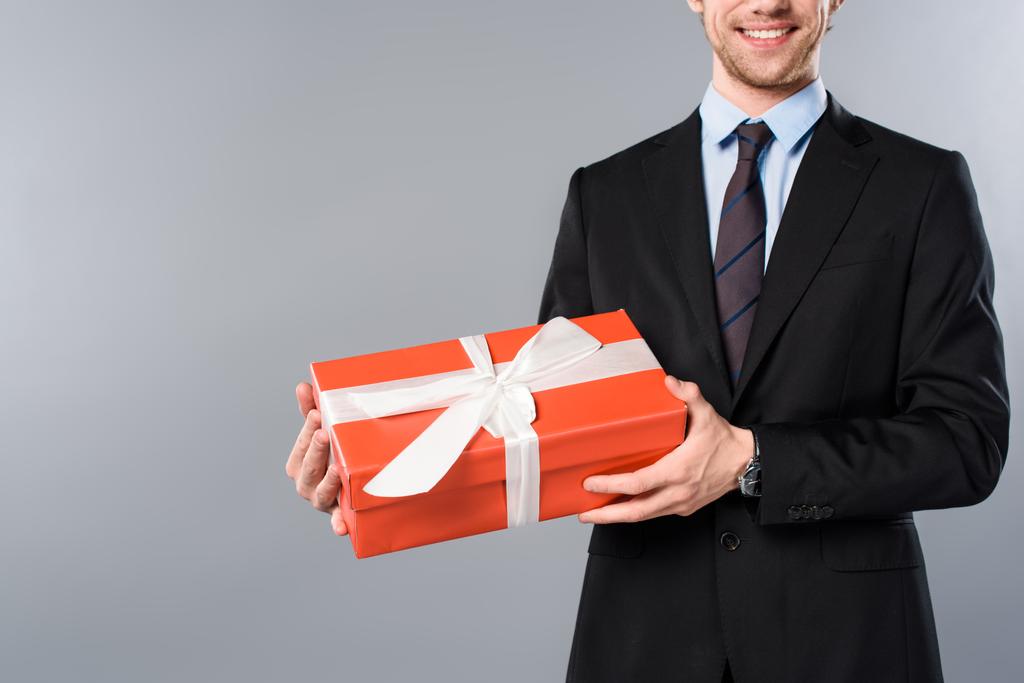 abgeschnittene Ansicht eines lächelnden Geschäftsmannes mit Geschenk auf grauem Hintergrund - Foto, Bild