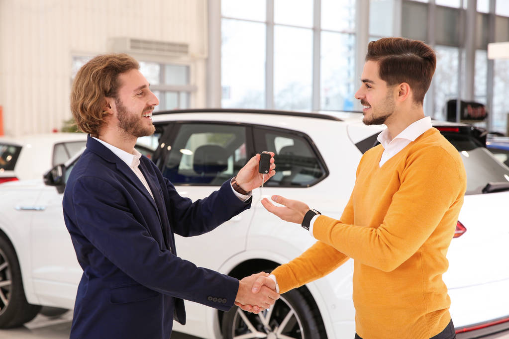Продавец автомобилей дает ключ клиенту во время рукопожатия в салоне
 - Фото, изображение