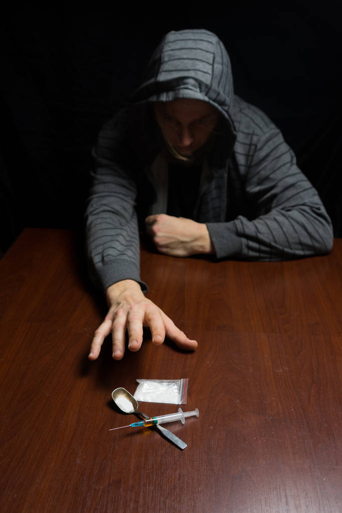 El adicto en la mesa tira de su mano a la jeringa con la dosis. Concepto contra las drogas
. - Foto, imagen