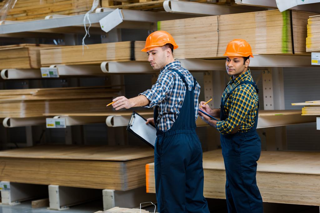two multicultural workers in uniform standing near wooden construction materials - Photo, Image