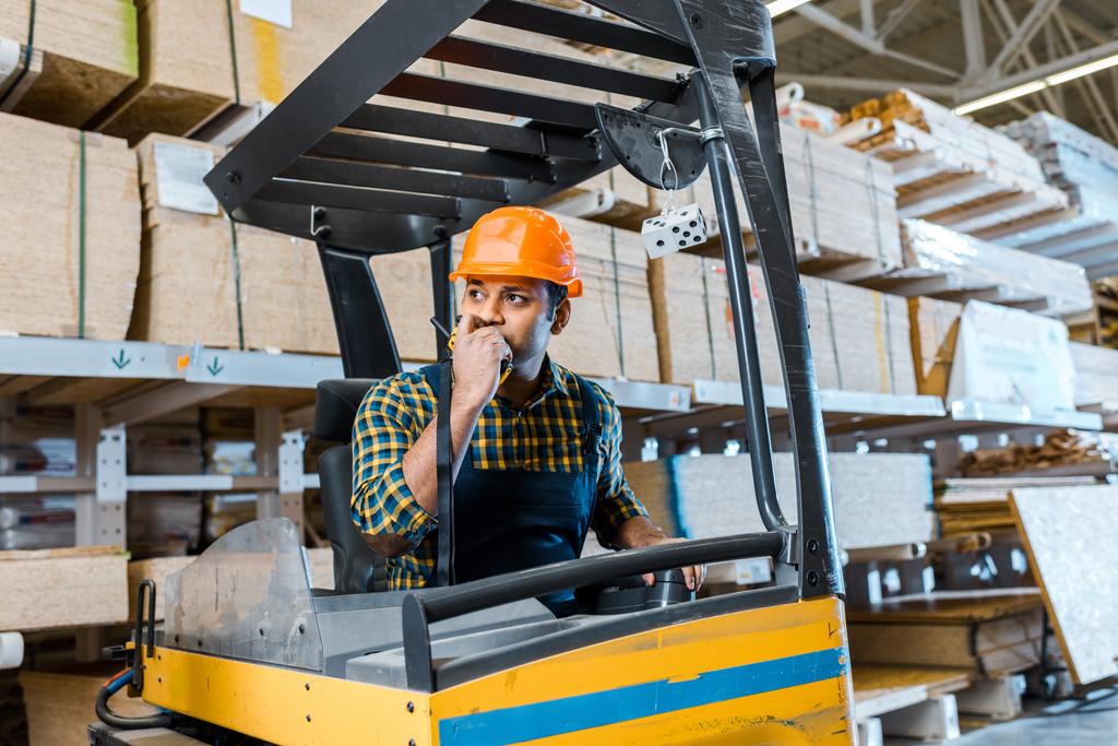 indian warehouse worker talking on walkie talkie while sitting in forklift machine - Photo, Image
