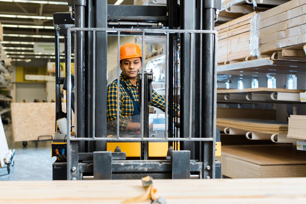 selective focus of handsome, conentrated indian worker sitting in forklift machine in warehouse - Photo, Image