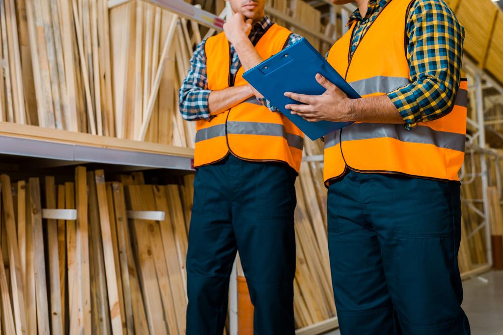 μερική όψη των εργαζομένων που στέκονται κοντά σε ράφια με ξύλινα κατασκευαστικά υλικά - Φωτογραφία, εικόνα