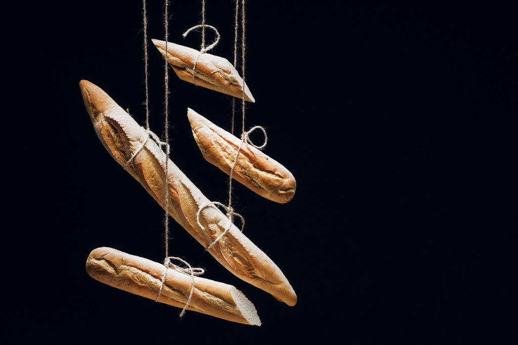 pães de baguetes frescos assados em cordas isoladas a preto
 - Foto, Imagem