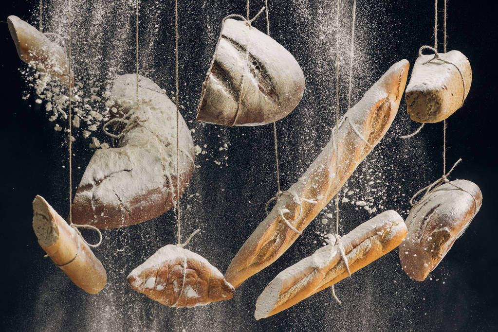 flour falling at fresh baked bread hanging on ropes on black background - Photo, Image