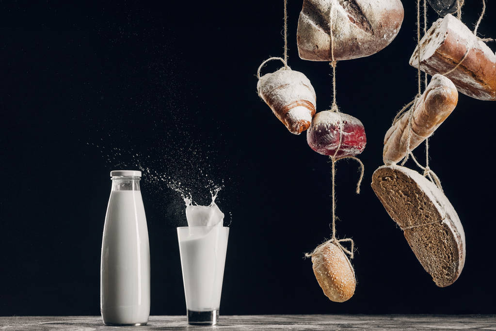 domácí chléb, visící na lanech poblíž stříkající mléko izolované na černém pozadí s kopií prostor - Fotografie, Obrázek