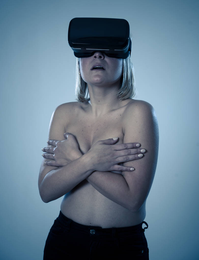 Mujer atractiva sensual usando gafas de realidad aumentada o virtual sintiéndose emocionada explorando la sexualidad virtual mientras se cubre el pecho en topless. En el simulador de sexo cibernético VR y nueva tecnología
. - Foto, imagen