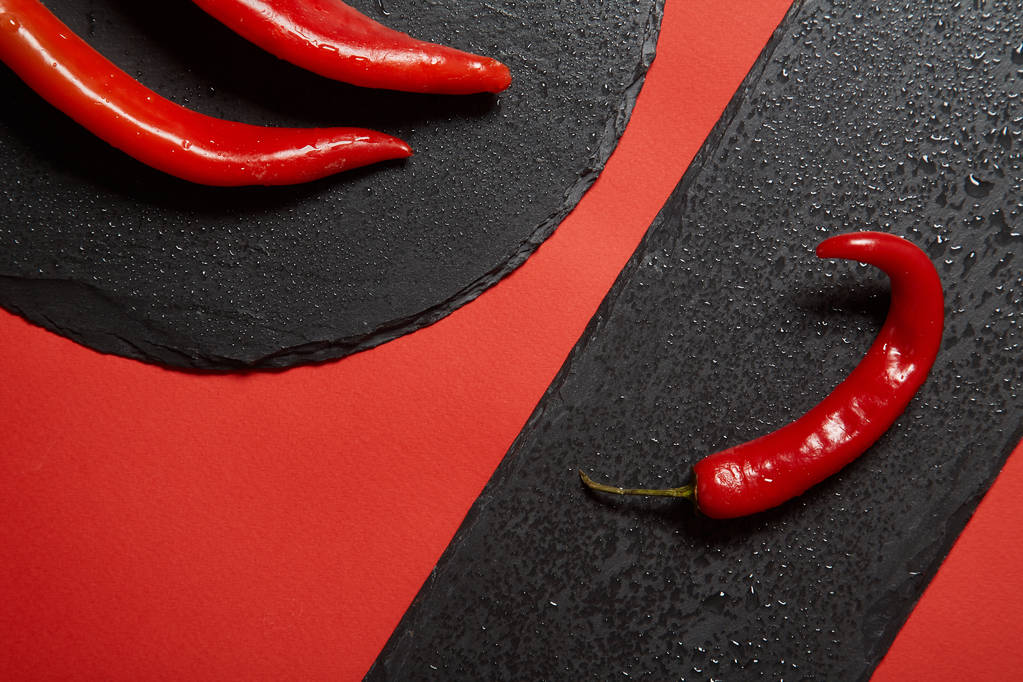 Κόκκινο καυτό πιπέρι τσίλι και κόκκινο peppper σε ένα μαύρο σχιστόλιθο πιάτο σε κόκκινο φόντο. - Φωτογραφία, εικόνα
