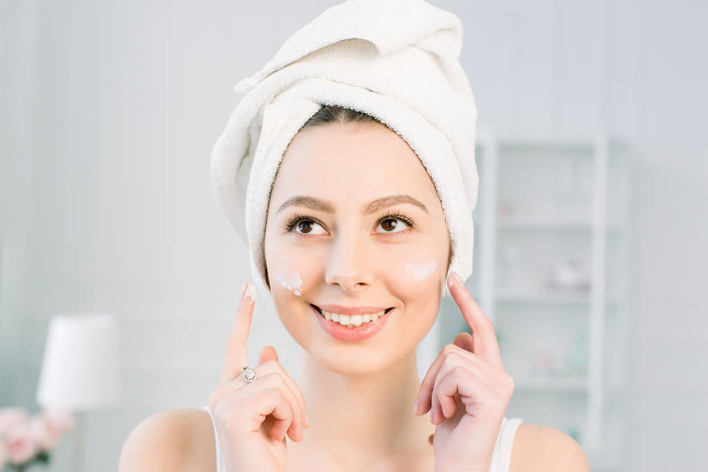 felice ragazza con un asciugamano sulla testa applicare una maschera detergente sul suo viso
 - Foto, immagini