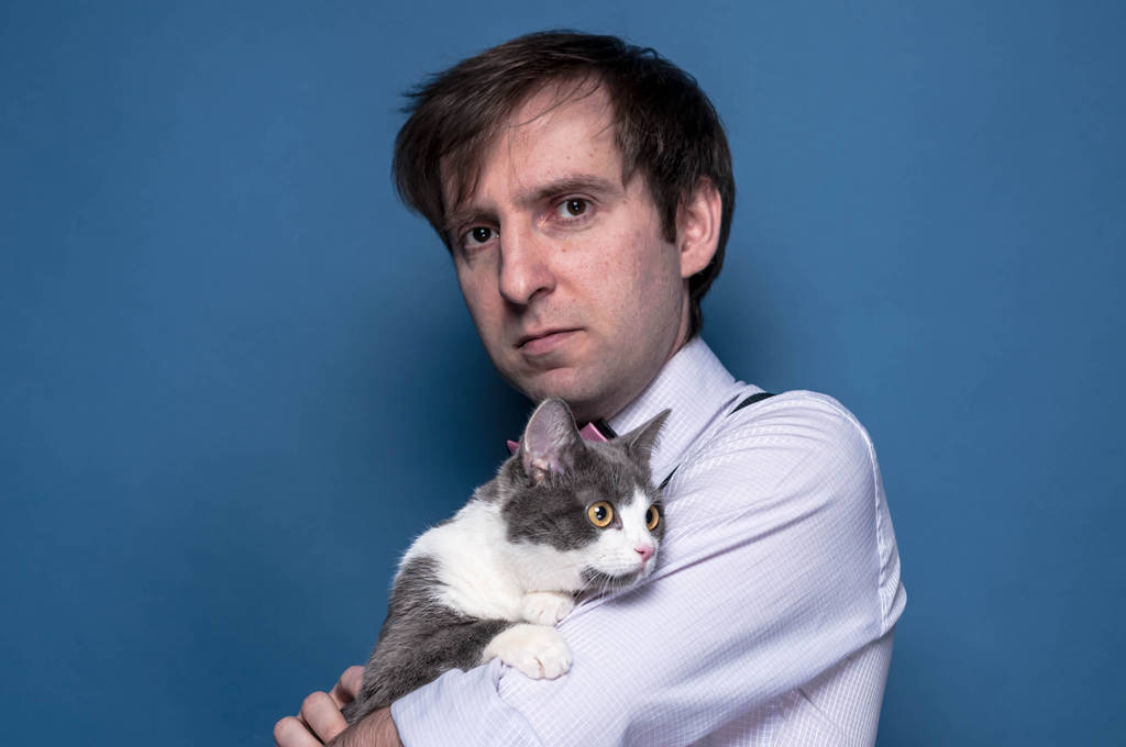 handsome man in shirt holding cute grey cat with white paws on blue background with copy space - Photo, Image