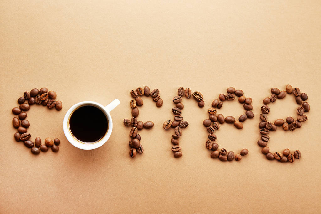 Word coffee spelled with roasted beans over creamy brown background. Close up, copy space, top view, flat lay. - Photo, Image
