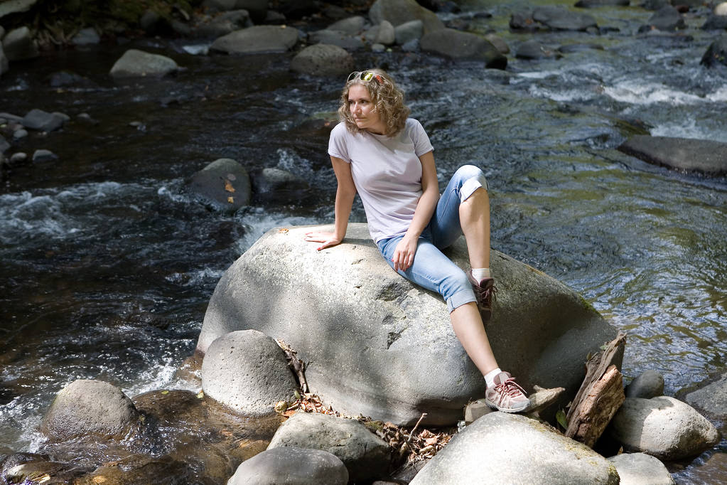 Uma bela jovem está sentada em uma pedra ao lado de uma montanha
 - Foto, Imagem