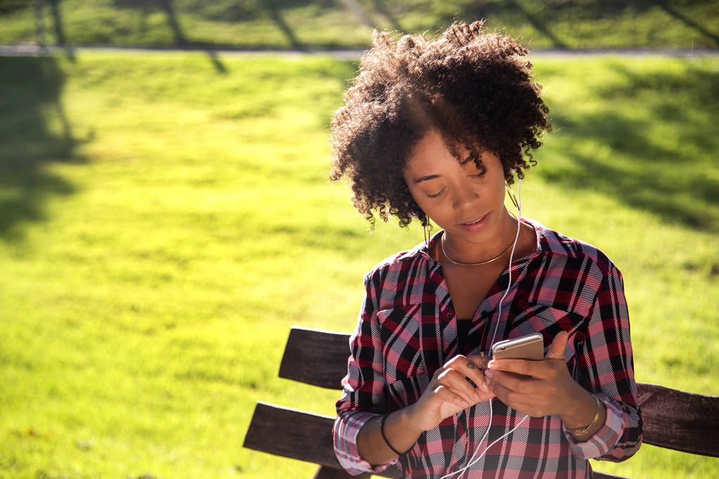 Portret van een jonge Afro-Amerikaanse vrouw luisteren naar muziek op mobiele telefoon-Imagem. - Foto, afbeelding