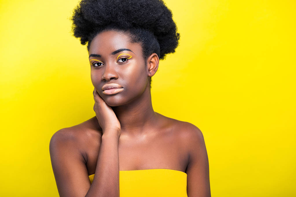 Atractiva mujer afroamericana con maquillaje de moda mirando a la cámara aislada en amarillo
 - Foto, Imagen