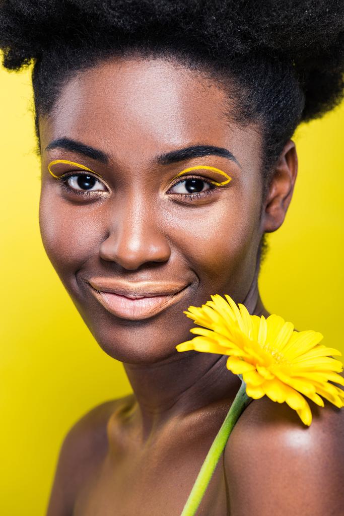 Χαμογελαστή Αφρικανική Αμερικάνικη κορίτσι κρατώντας λουλούδι απομονώνεται σε κίτρινο - Φωτογραφία, εικόνα