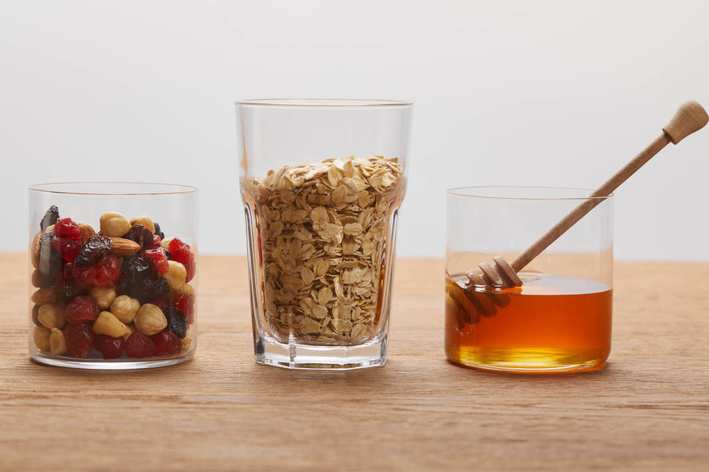 vasos con bayas secas, frutos secos, copos de avena y miel sobre mesa de madera aislada en gris
 - Foto, imagen