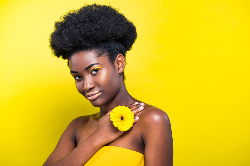 Досить афроамериканець дівчина з квіткою дивлячись на камеру на жовтому - Фото, зображення