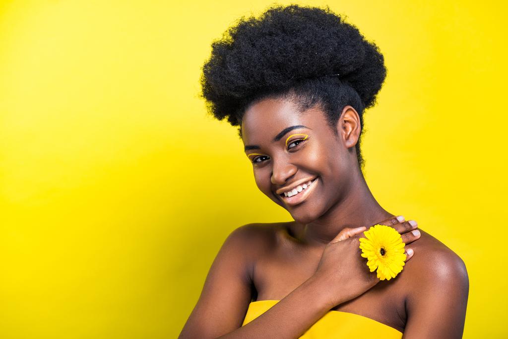 Cheerful smiling african american woman with flower on yellow - Photo, Image