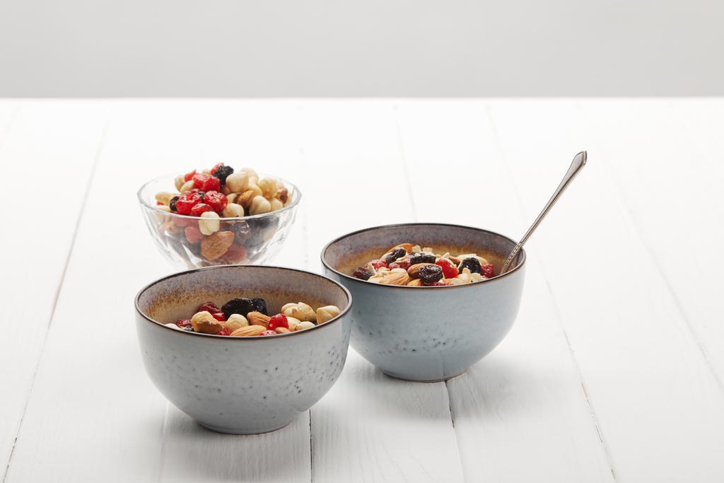 kommen met muesli, gedroogde bessen en noten geserveerd voor het ontbijt op witte tafel geïsoleerd op grijs - Foto, afbeelding