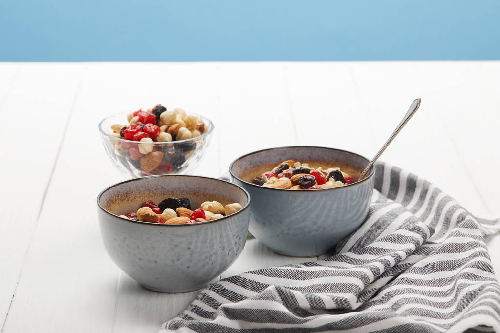 miski z muesli, suszone jagody i orzechy serwowane na śniadanie w pobliżu pasiasty serwetki izolowane na niebiesko - Zdjęcie, obraz