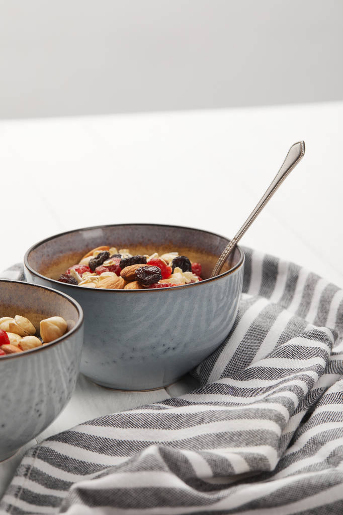 bols avec muesli, baies séchées et noix servis pour le petit déjeuner près de tissu rayé isolé sur gris
 - Photo, image
