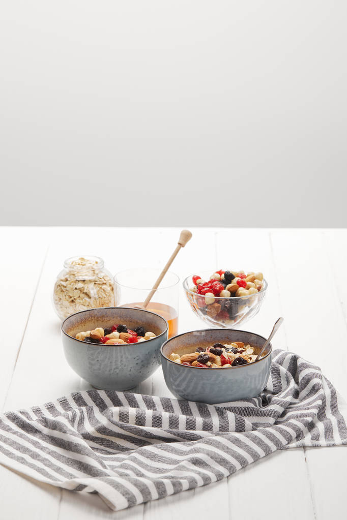 kommen met muesli, gedroogde bessen en noten geserveerd voor het ontbijt met honing geïsoleerd op grijs - Foto, afbeelding