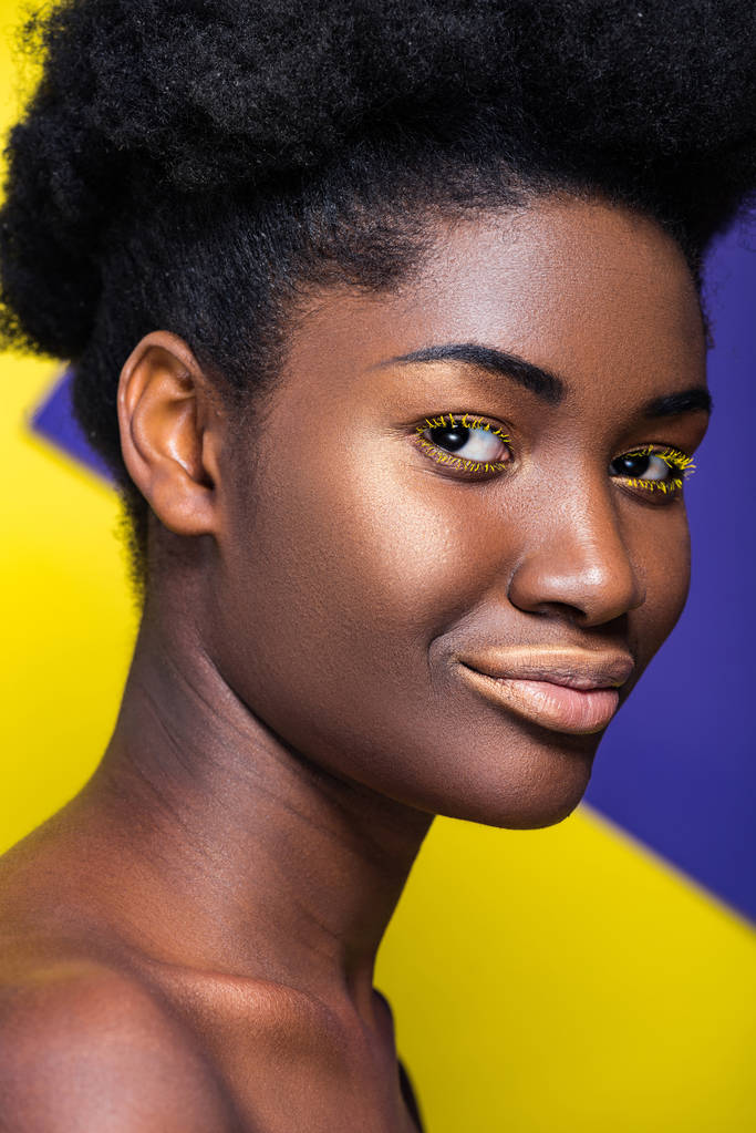 Sonriente mujer afroamericana bastante mirando a la cámara en amarillo y púrpura
 - Foto, imagen