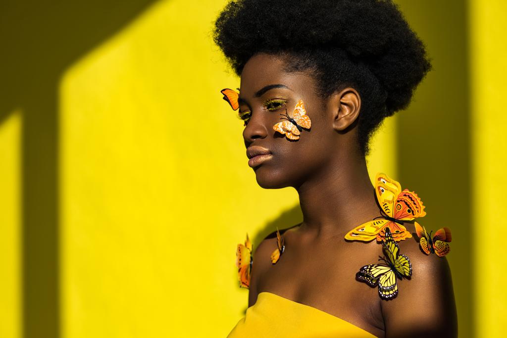 Ελκυστική αφρικανική αμερικανική νεαρή γυναίκα με πεταλούδες στο κίτρινο - Φωτογραφία, εικόνα
